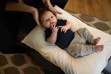 A baby lying on their back on a pillow, with a doctor's hands gently at their head