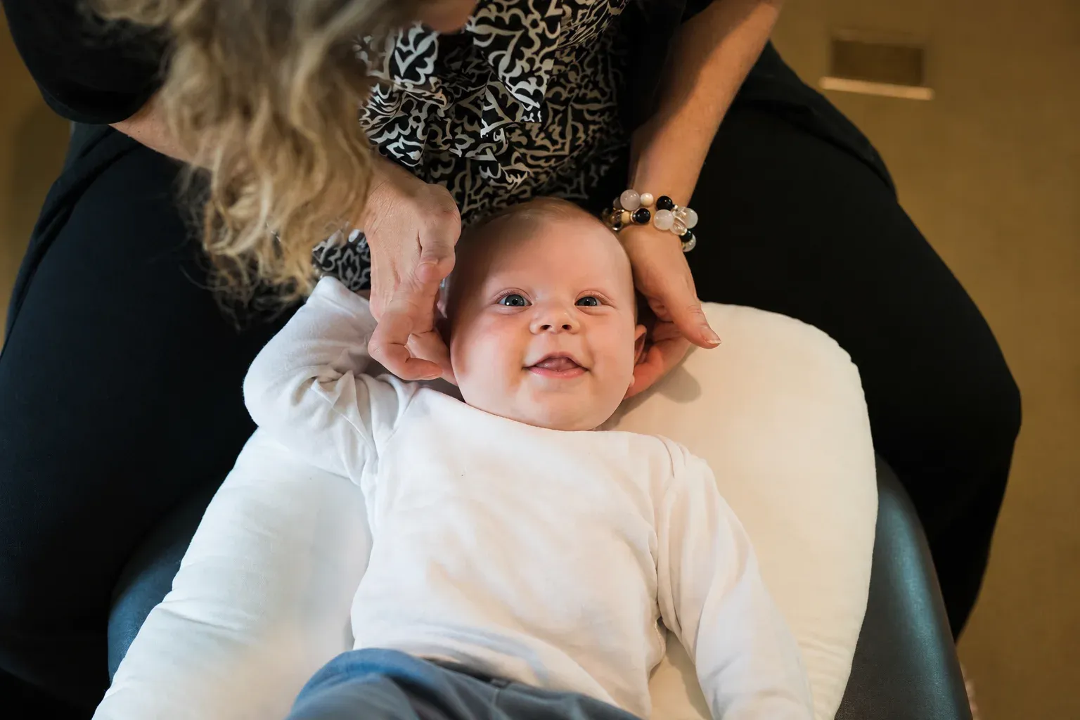 A smiling baby lies on a pillow while a doctor gently supports their head